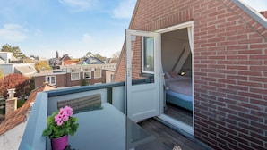 A bedroom with a bed, a window, and a balcony with a potted plant. - Boutique Pension Bennekom - Studio 4 (Zandvoort)