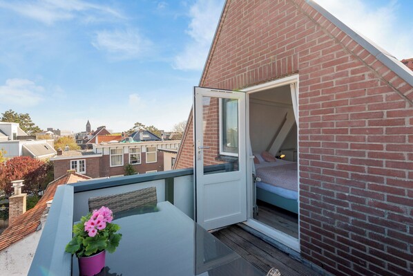 A bedroom with a bed, a window, and a balcony with a potted plant. - Boutique Pension Bennekom - Studio 4 (Zandvoort)