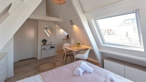 A bedroom with a bed, a desk, a chair, a small table, a mirror, and a window. - Boutique Pension Bennekom - Studio 4 (Zandvoort)