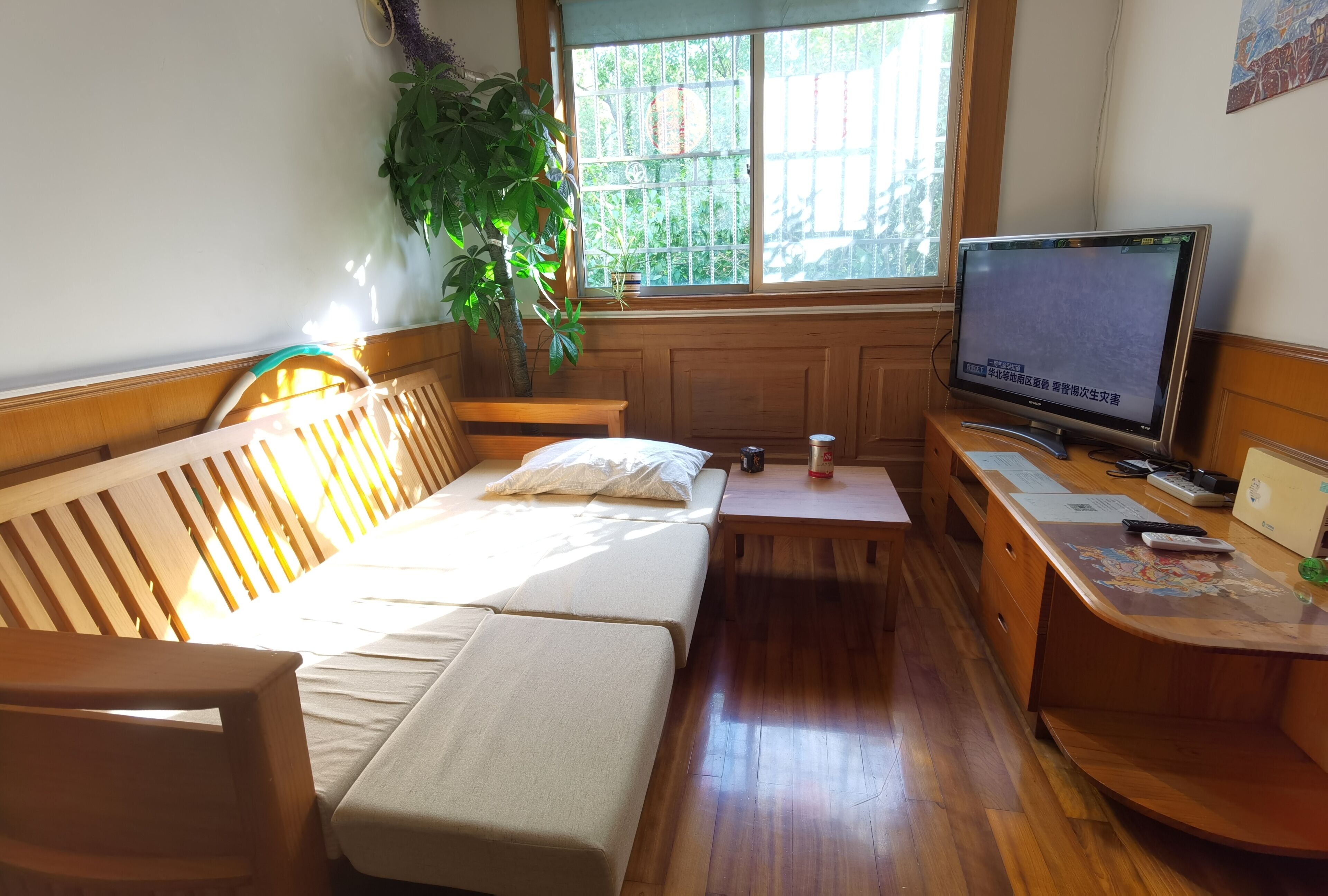 A small, cozy room with a wooden bed, a desk with a computer, and a window with a view of greenery.