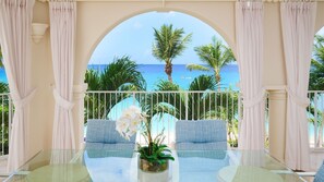 Ein Balkon mit Glastisch, zwei gepolsterten Stühlen, einem Blumentopf und Blick aufs Meer.
