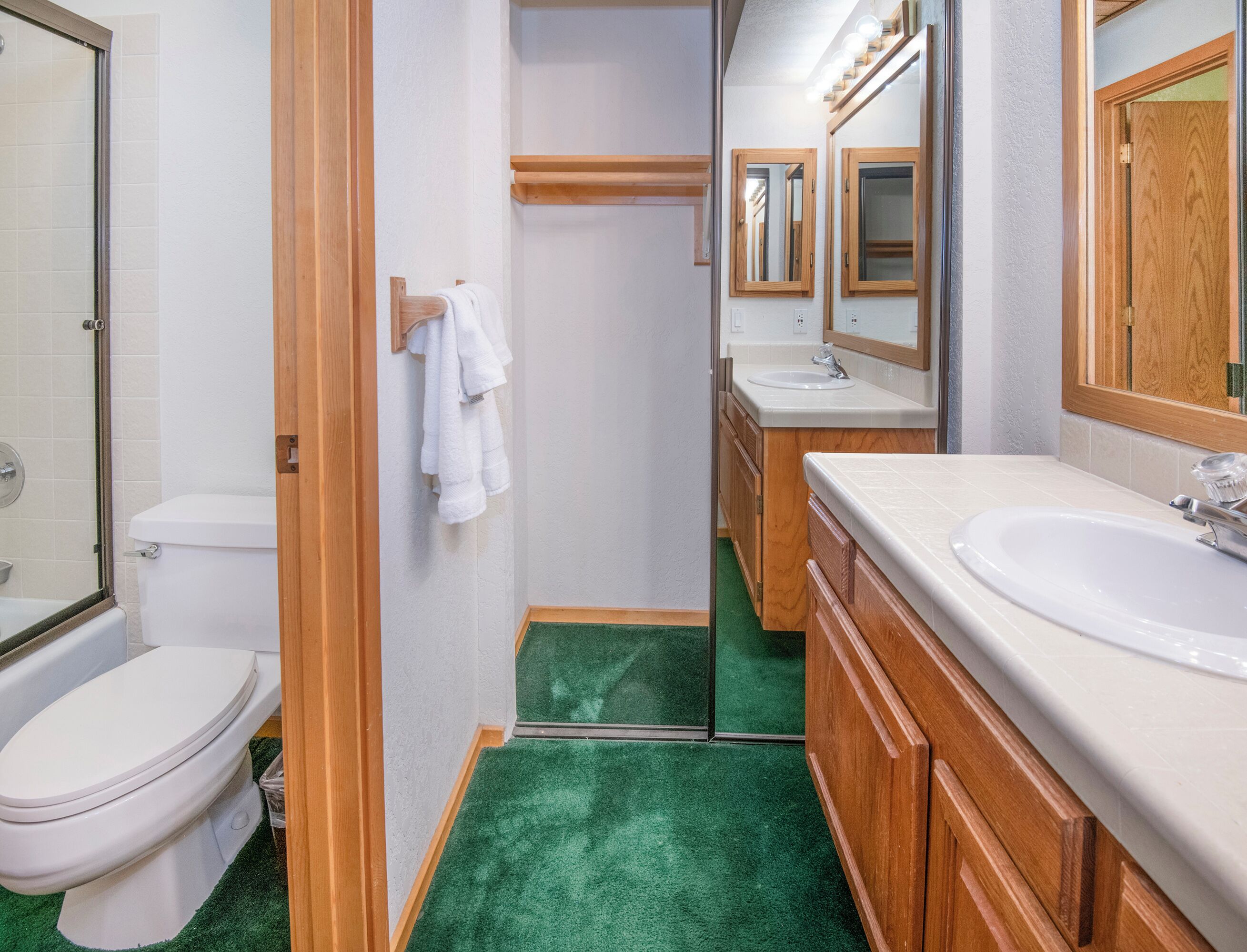 A bathroom with a toilet, sink, mirror, and green carpet.