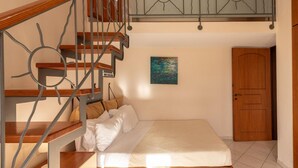 Un dormitorio con una escalera de madera, una cama con ropa blanca, un cuadro en la pared y una puerta de madera.
