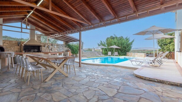 Un patio exterior con suelo de piedra, una parrilla y una zona de piscina con tumbonas y sombrillas.