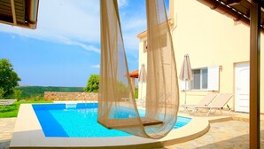 Una piscina con cubierta de piedra, una pérgola con toldo de malla y sillones de descanso.