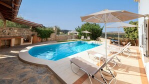 Una piscina con sillones de descanso y sombrillas, rodeada de muros de piedra y vegetación.