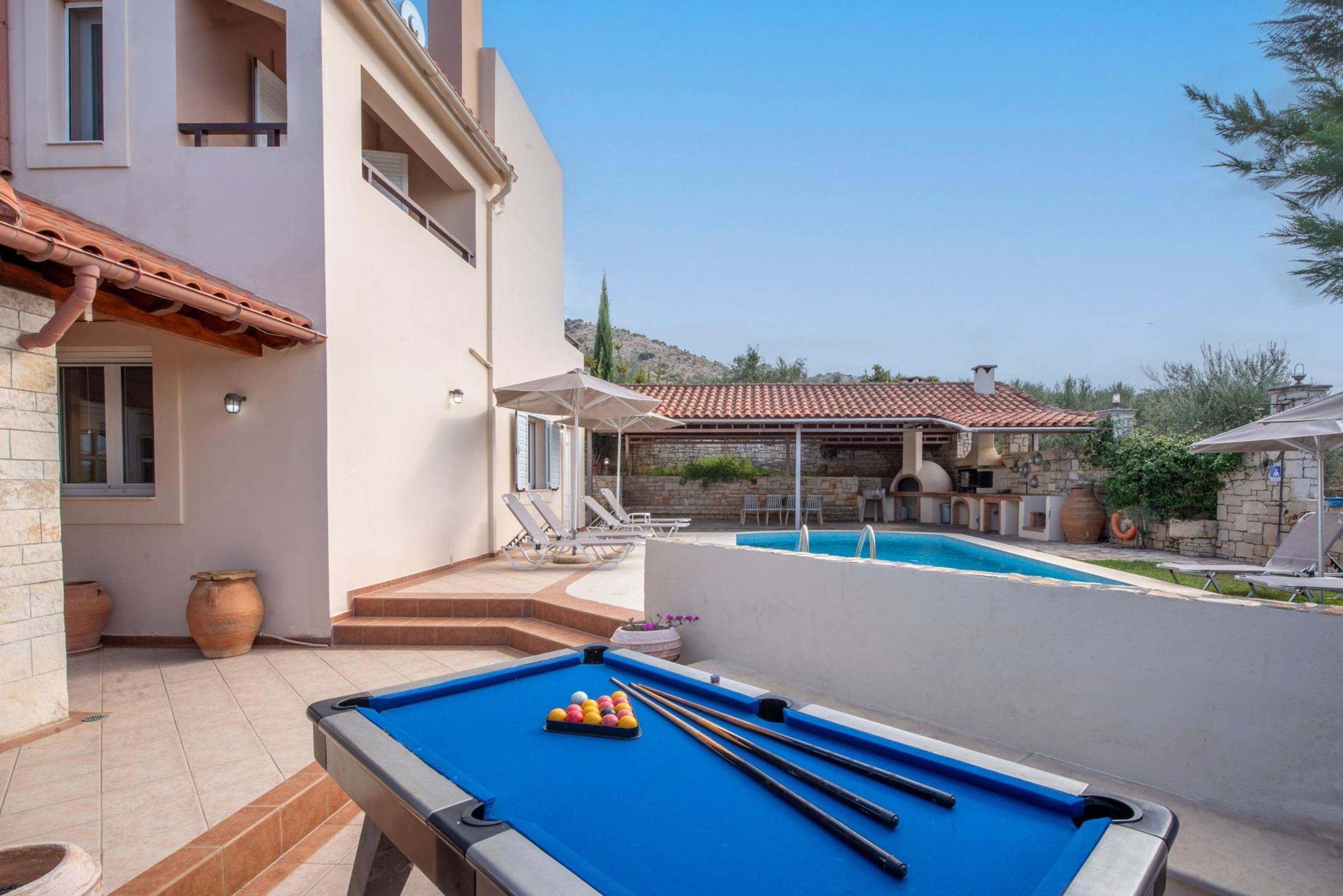A pool table with billiard balls, a pool, and lounge chairs in a courtyard.