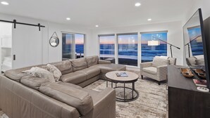 Ein modernes Wohnzimmer mit einem großen Ecksofa, einem runden Couchtisch und Meerblick durch große Fenster.