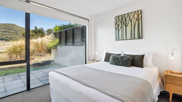 Une chambre avec un grand lit, une porte vitrée donnant sur un balcon et un tableau accroché au mur.
