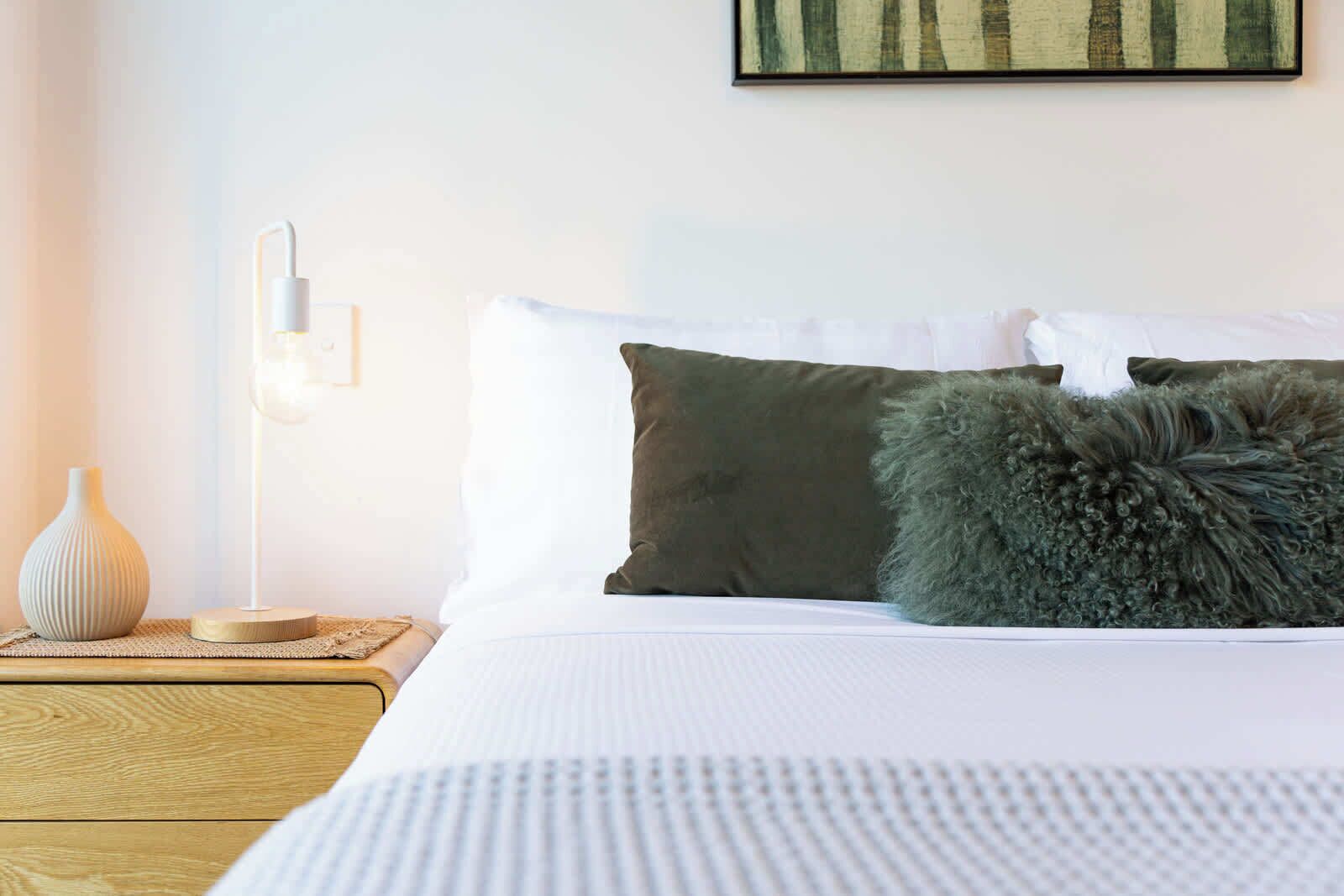 Una cama bien hecha con ropa blanca y dos almohadas, una verde y otra mullida.