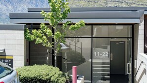 Un bâtiment moderne avec une entrée en verre, portant l’inscription « APPARTEMENTS 11-22 », et offrant une vue sur les montagnes en arrière-plan.