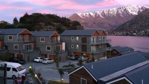 A row of modern multi-story buildings with balconies, a parking area, and a view of a lake and mountains in the background. - Lakefront, Mountain Views, Stylish unit (Queenstown)