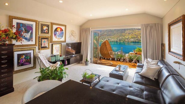 A living room with a large TV, comfortable seating, a dining table, and a view of a body of water. - Lakefront, Mountain Views, Stylish unit (Queenstown)