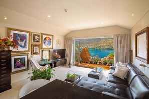 A living room with a large TV, comfortable seating, a dining table, and a view of a body of water.
