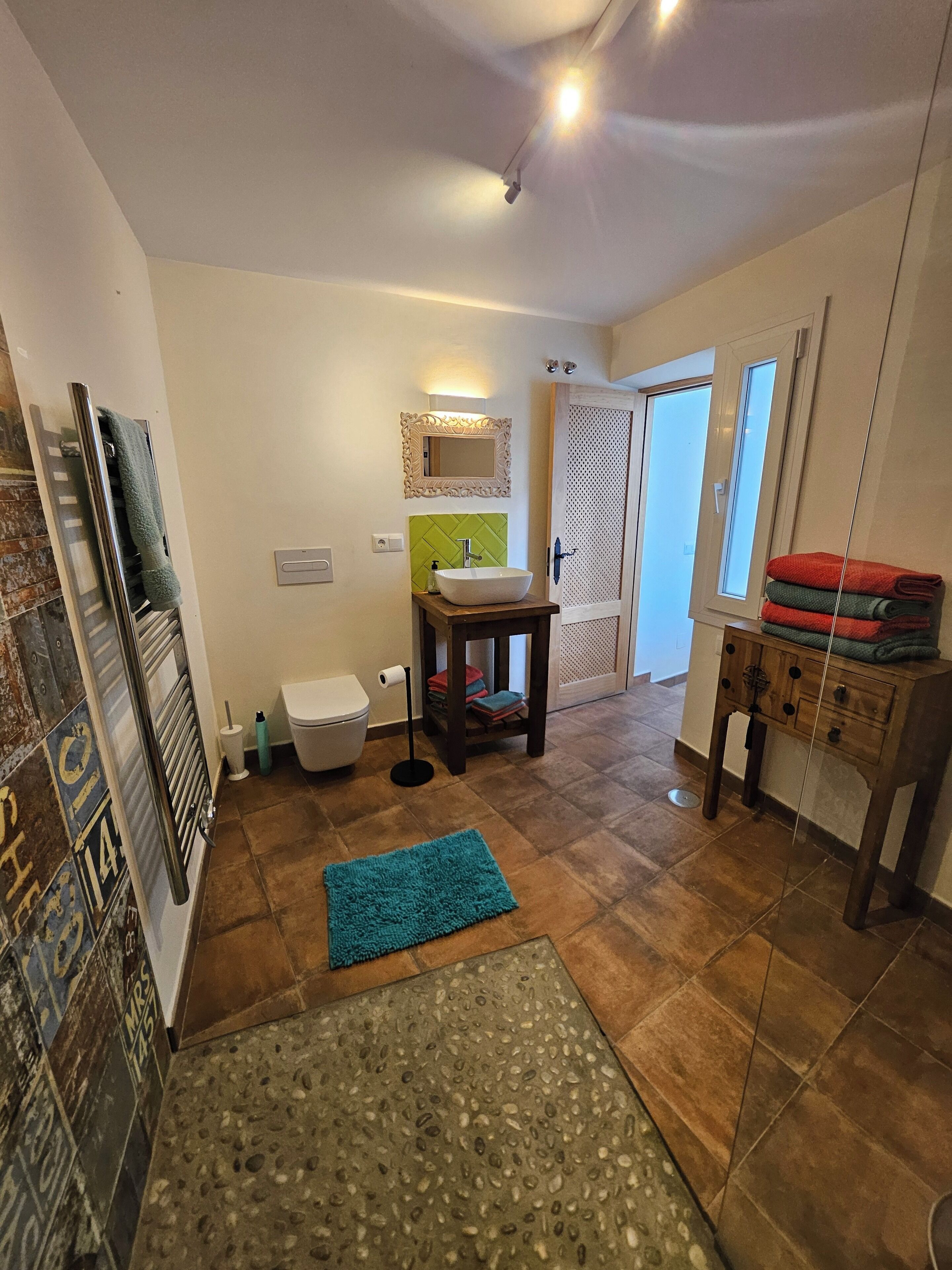 A bathroom with a white sink, green wall tiles, a towel rack, a toilet, and a mirror.