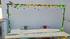 Une terrasse avec une table et des chaises carrelées, entourée d’un mur blanc et d’une pergola en bois.