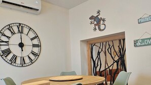 Un coin repas avec une table ronde en bois, des chaises vertes, une grande horloge murale et une branche d’arbre décorative fixée au mur.