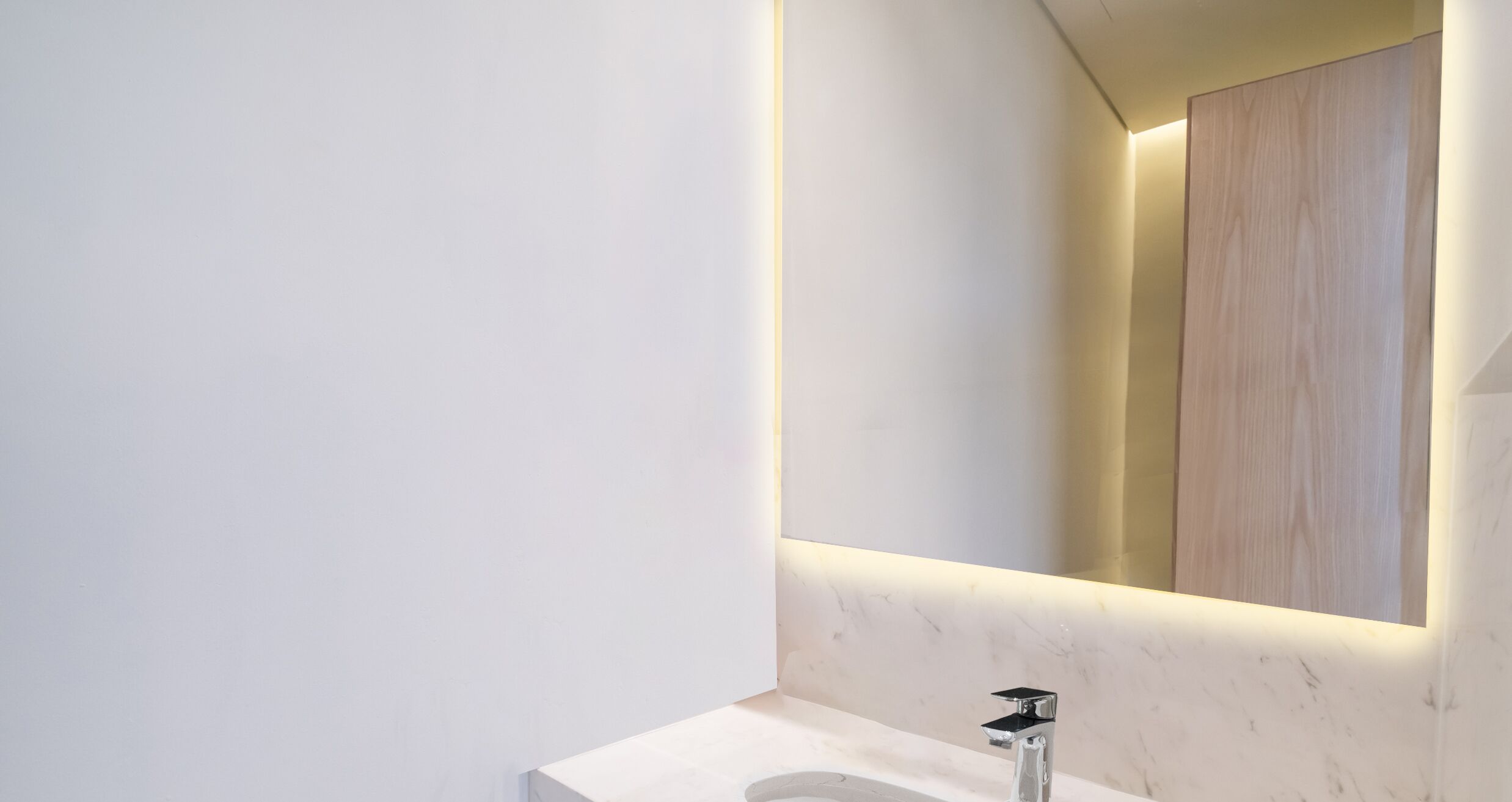 A modern bathroom with a marble countertop, a single sink, and a mirror with integrated lighting.