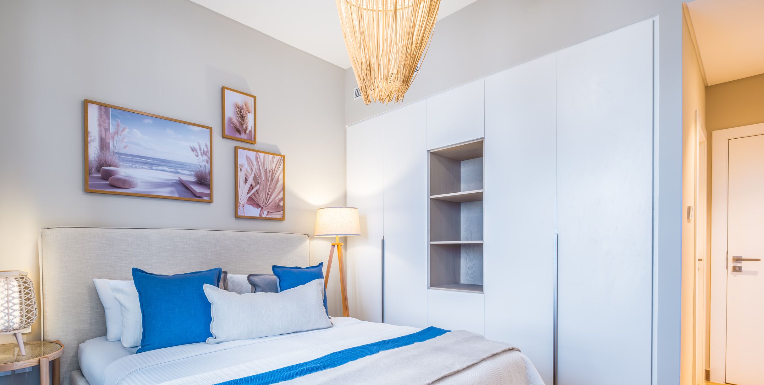 A modern hotel room with a large bed, a nightstand, a lamp, and wall-mounted shelves.