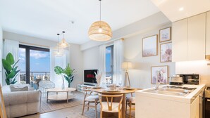 A modern living room with a sofa, dining table, and chairs, a TV, and a kitchen area with a sink and appliances. - LUX  La Mer Infinity View-Luxury Boho 1 (Dubai)