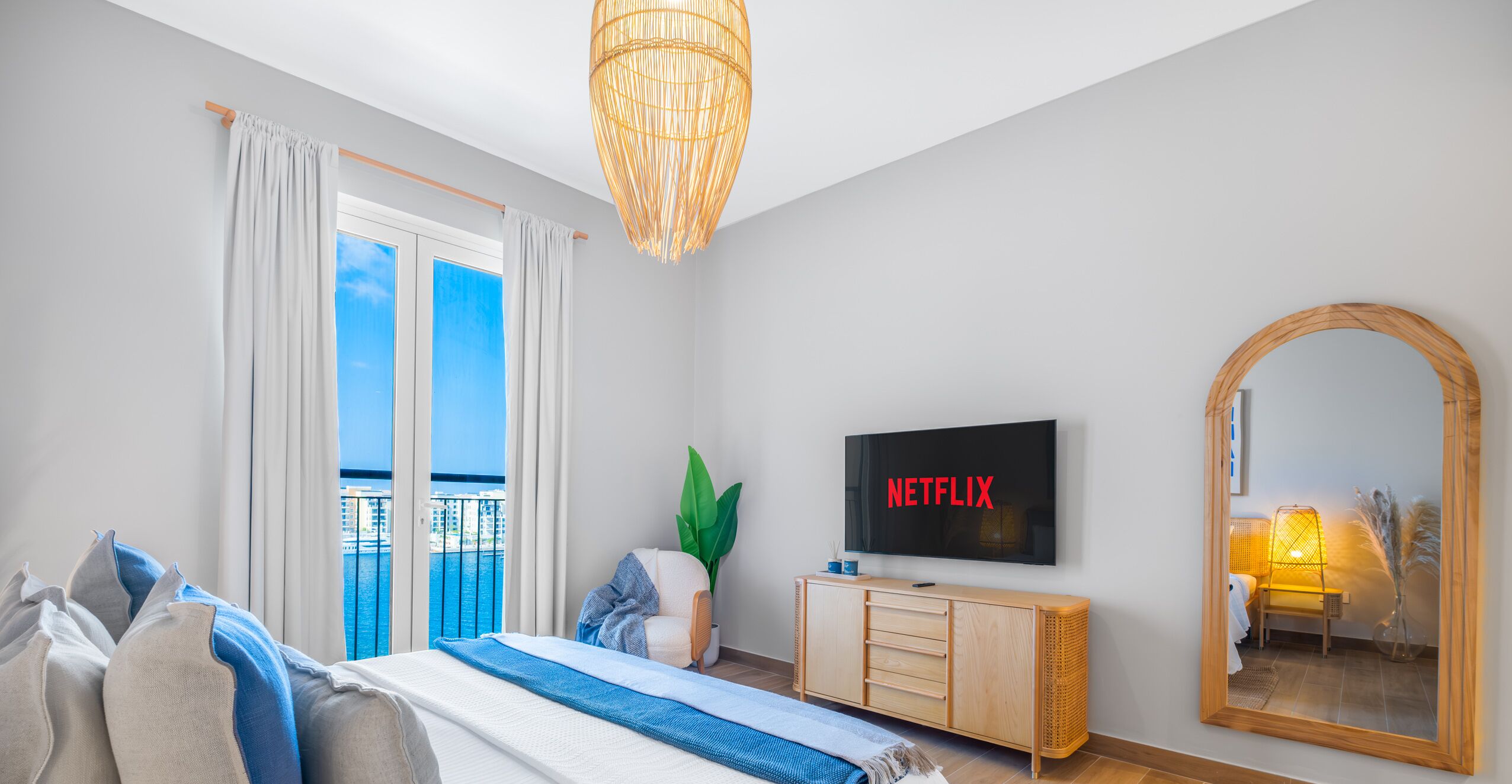 Een moderne slaapkamer met een groot bed, een televisie, een spiegel en een balkon met uitzicht op zee.