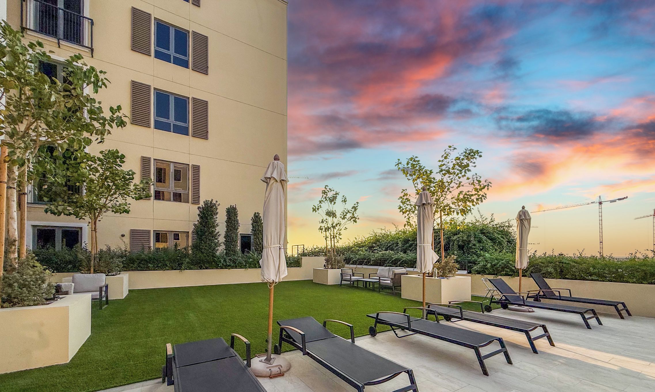 A rooftop patio with lounge chairs and umbrellas, a well-maintained lawn, and a building with multiple windows and shutters.