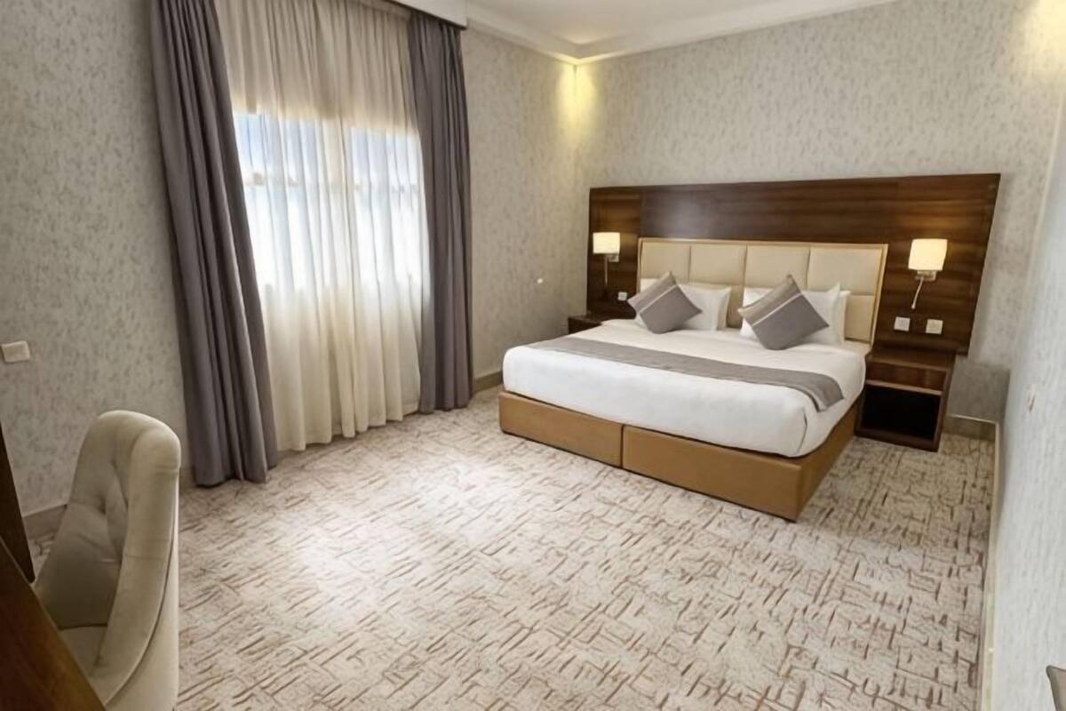 A hotel room with a large bed, a chair, a nightstand, and a window with curtains.