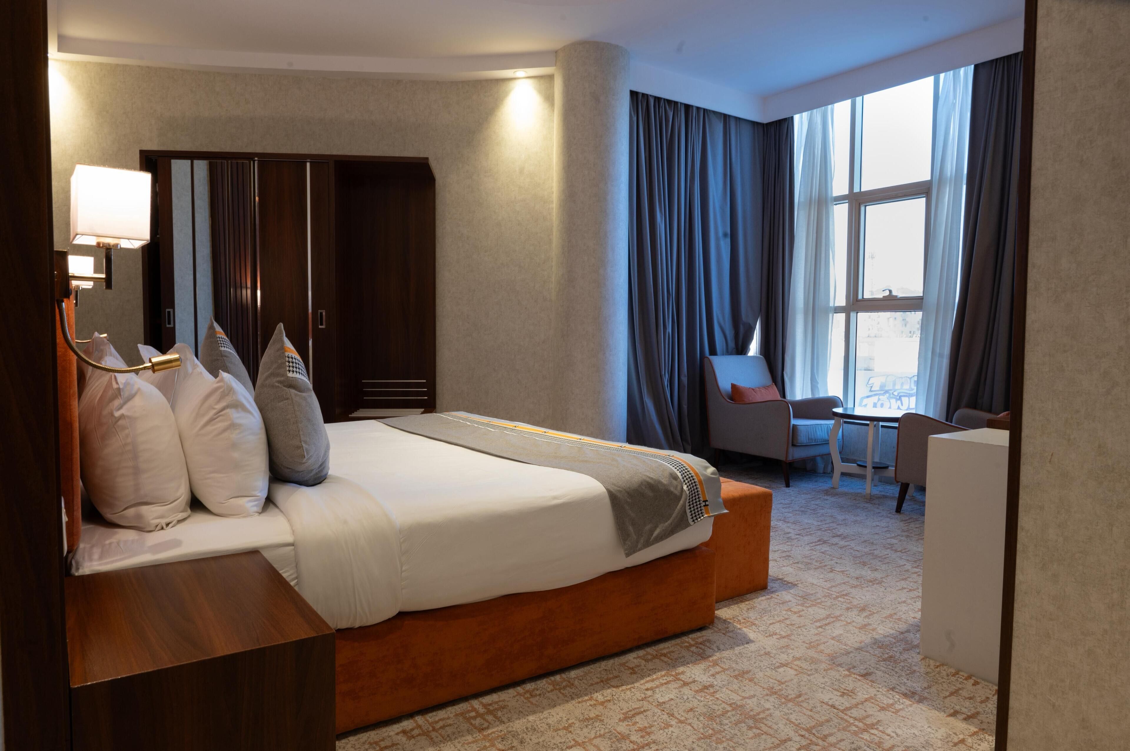 A hotel room with a large bed, a desk, a chair, and a wardrobe.