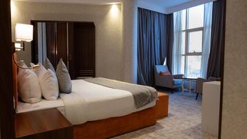 A hotel room with a large bed, a desk, a chair, and a wardrobe.