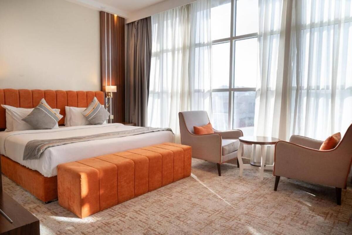 A hotel room with a large bed, a sitting area with two chairs, a small table, and a large window with curtains.