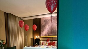 Une chambre d’hôtel moderne avec une grande baignoire, un lit décoré avec le mot « Amour » et des ballons en forme de cœur rouge.