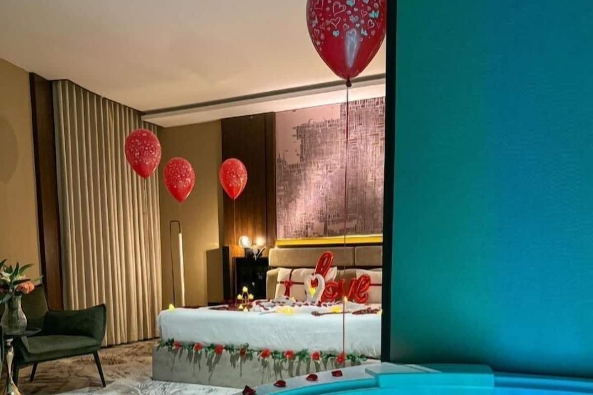 A modern hotel room with a large bathtub, a bed with a 'Love' decoration, and red heart balloons.