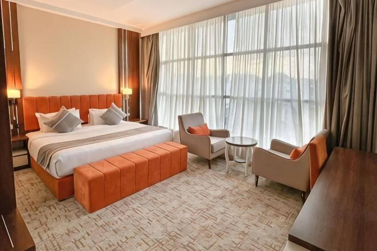 A hotel room with a large bed, a seating area with a chair and a small table, and a large window with curtains.