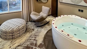 Une salle de bain moderne avec une grande baignoire, un banc rembourré, un fauteuil à bascule et une vue sur une mosquée par la fenêtre.