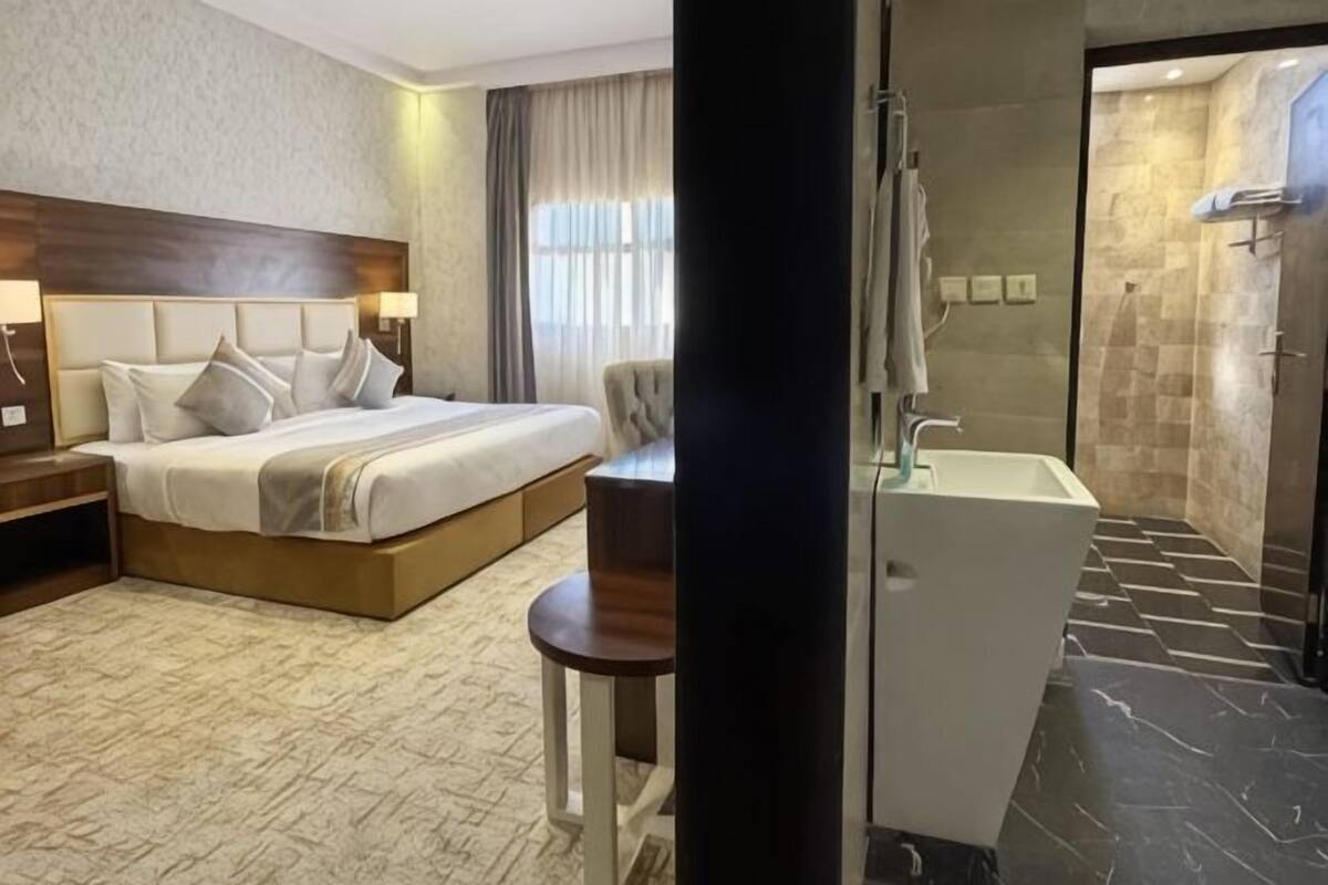 A hotel room with a bed, bedside table, lamp, and a bathroom with a shower and sink.