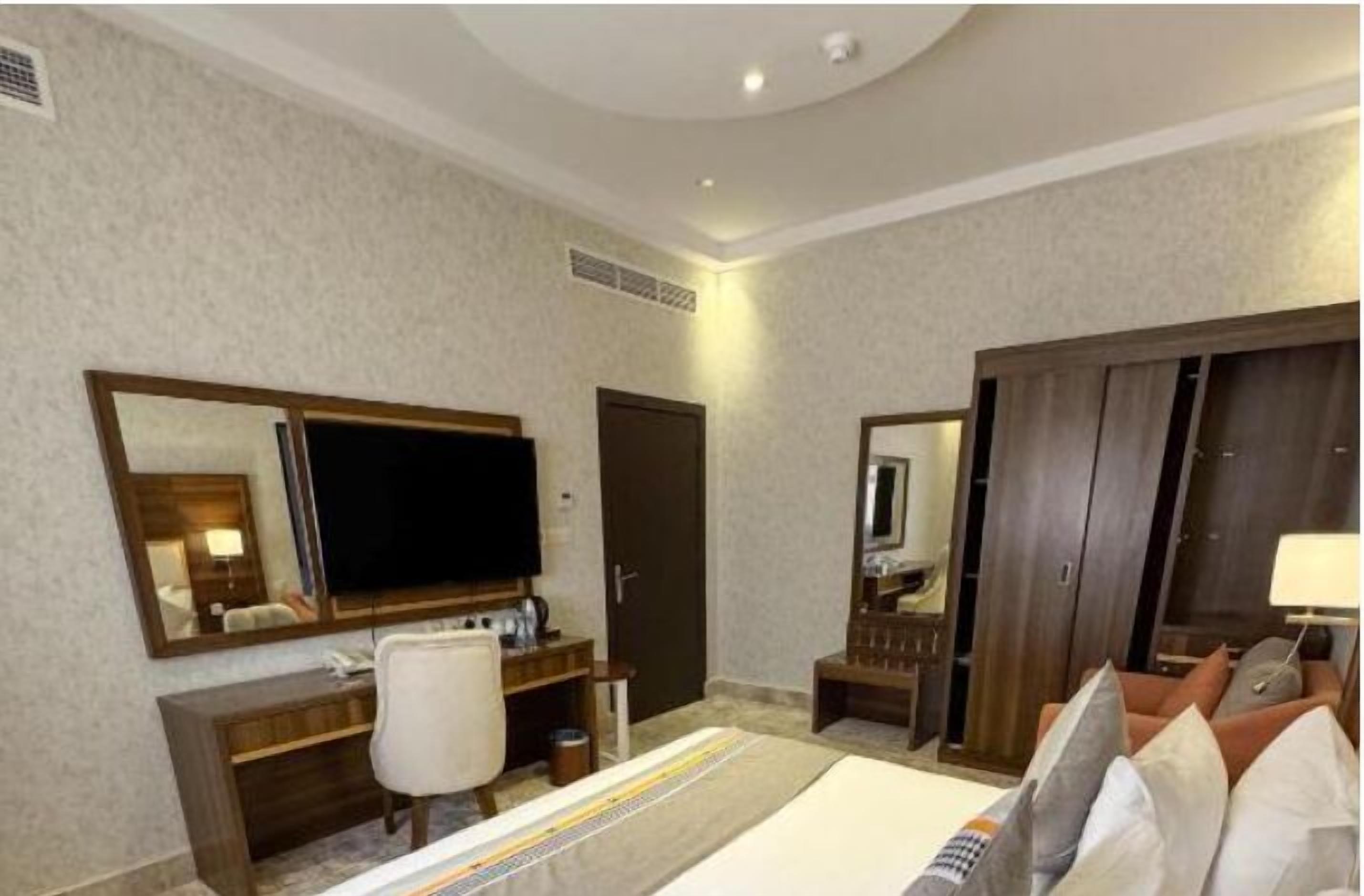 A hotel room with a large bed, a desk with a chair, a TV, a wardrobe, and a mirror.