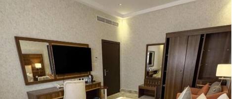 A hotel room with a large bed, a desk with a chair, a TV, a wardrobe, and a mirror.