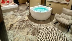 Une salle de bain moderne avec une baignoire sur pieds, un grand miroir et un coin salon agrémenté d’un pouf à motifs.