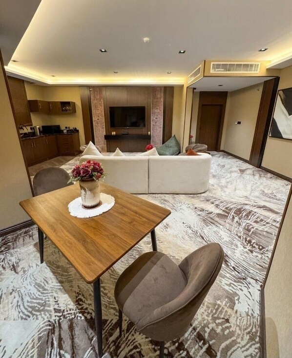 A modern living room with a sofa, a dining table with a vase of flowers, and a TV mounted on the wall.