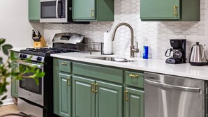 A kitchen with green cabinets, a stainless steel dishwasher, a microwave, a gas stove, and a coffee maker. - Colorful 5BR 3BA in Oakland, near Pitt & CMU (Pittsburgh)
