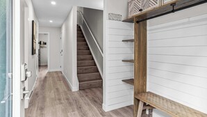 Un pasillo con una escalera de madera, paredes blancas y un banco.