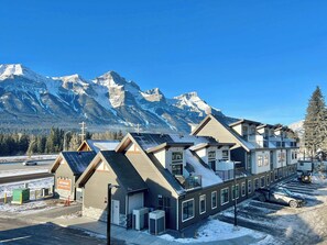 A hotel with multiple buildings, a parking area, and a view of snow-covered mountains. - Brand New - Mt Rundle Views 3 Bd Townhome (Harvie Heights)