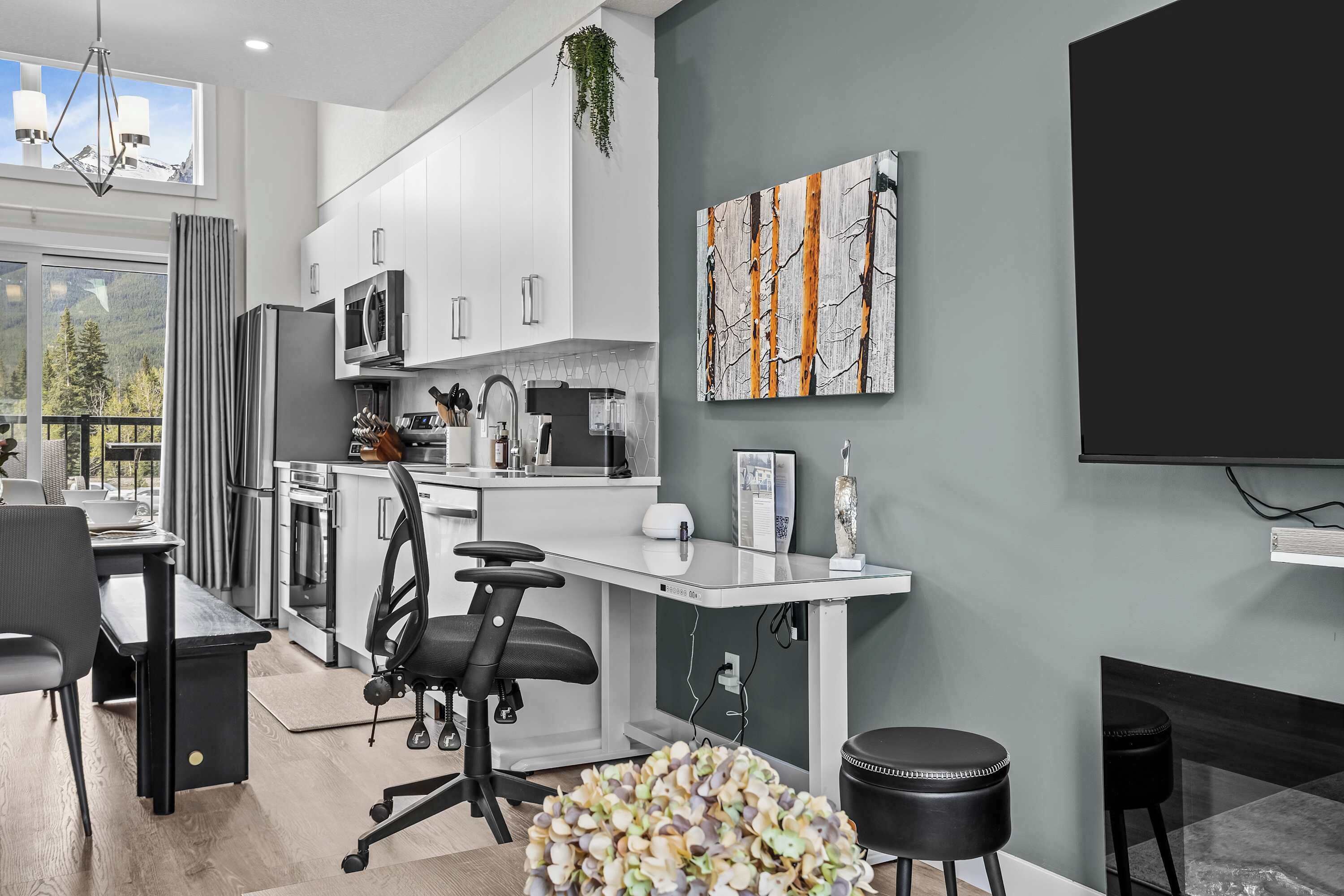 A modern kitchen with white cabinets, a black countertop, and a dining area with a black chair and table.