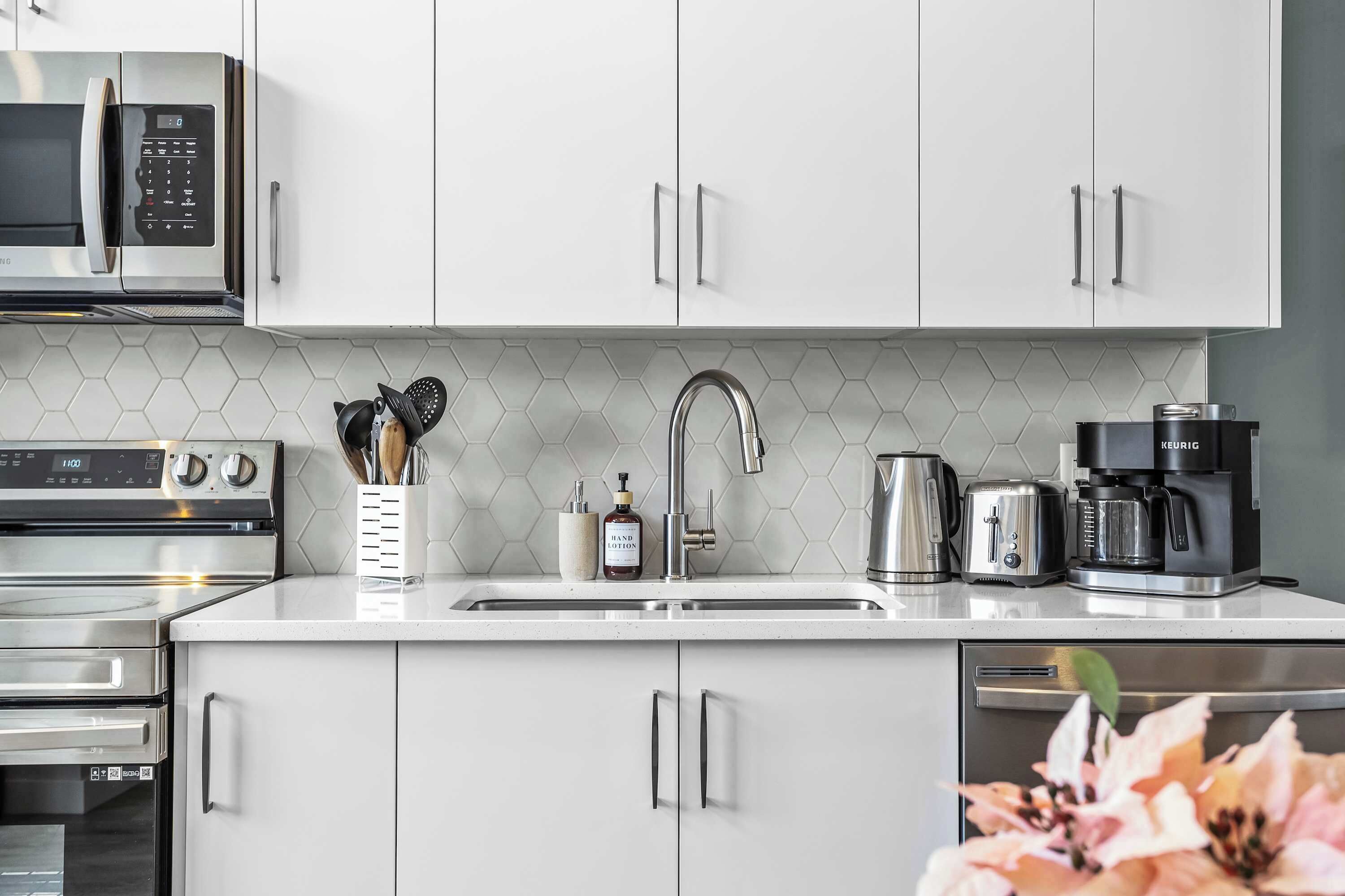 Une cuisine moderne avec des meubles blancs, des appareils en acier inoxydable, un four à micro-ondes, un four, un grille-pain et une machine à café.