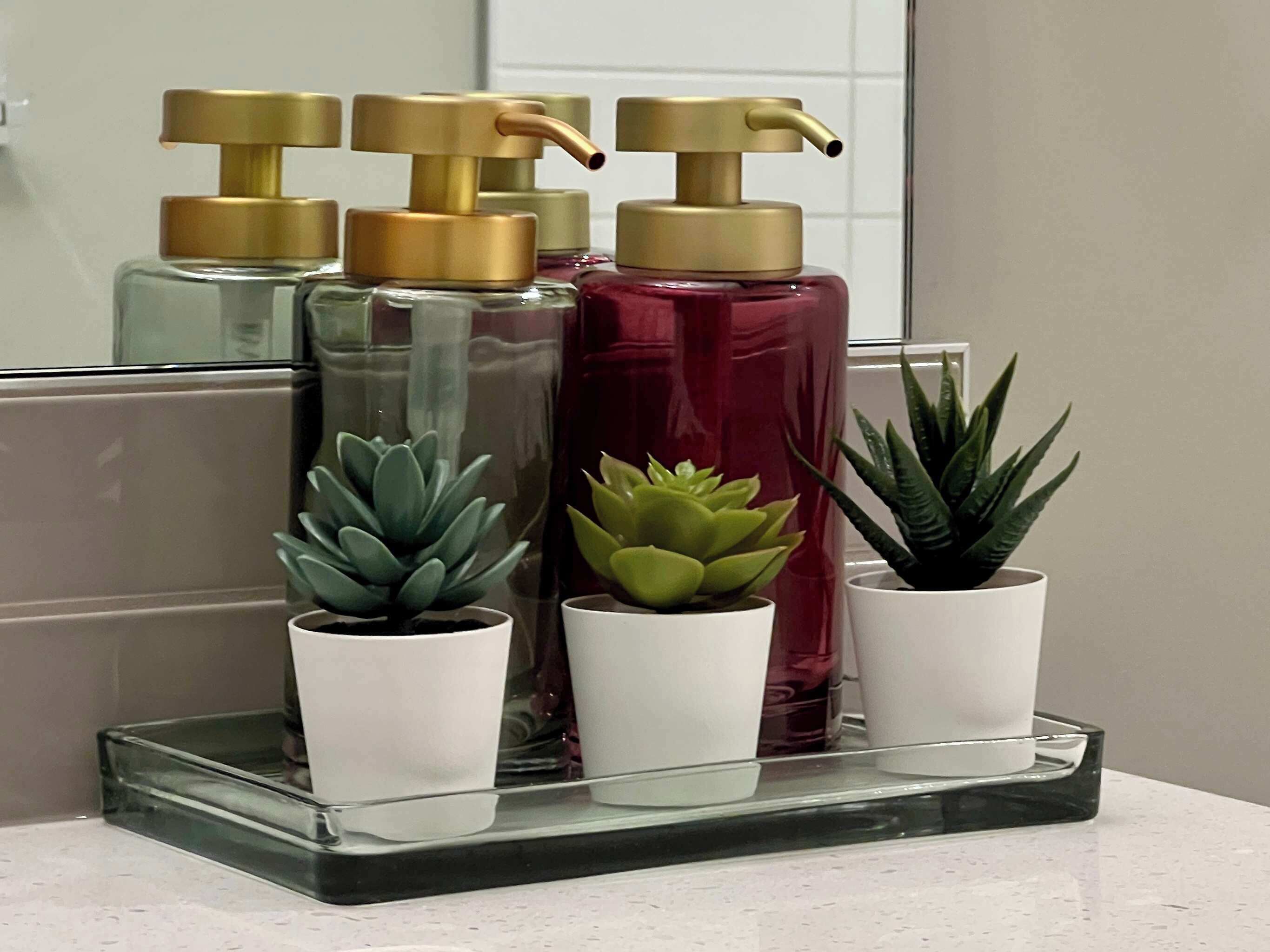 Una repisa en el baño con tres botellas de jabón líquido y tres suculentas en macetas.