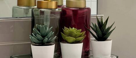 Una repisa en el baño con tres botellas de jabón líquido y tres suculentas en macetas.