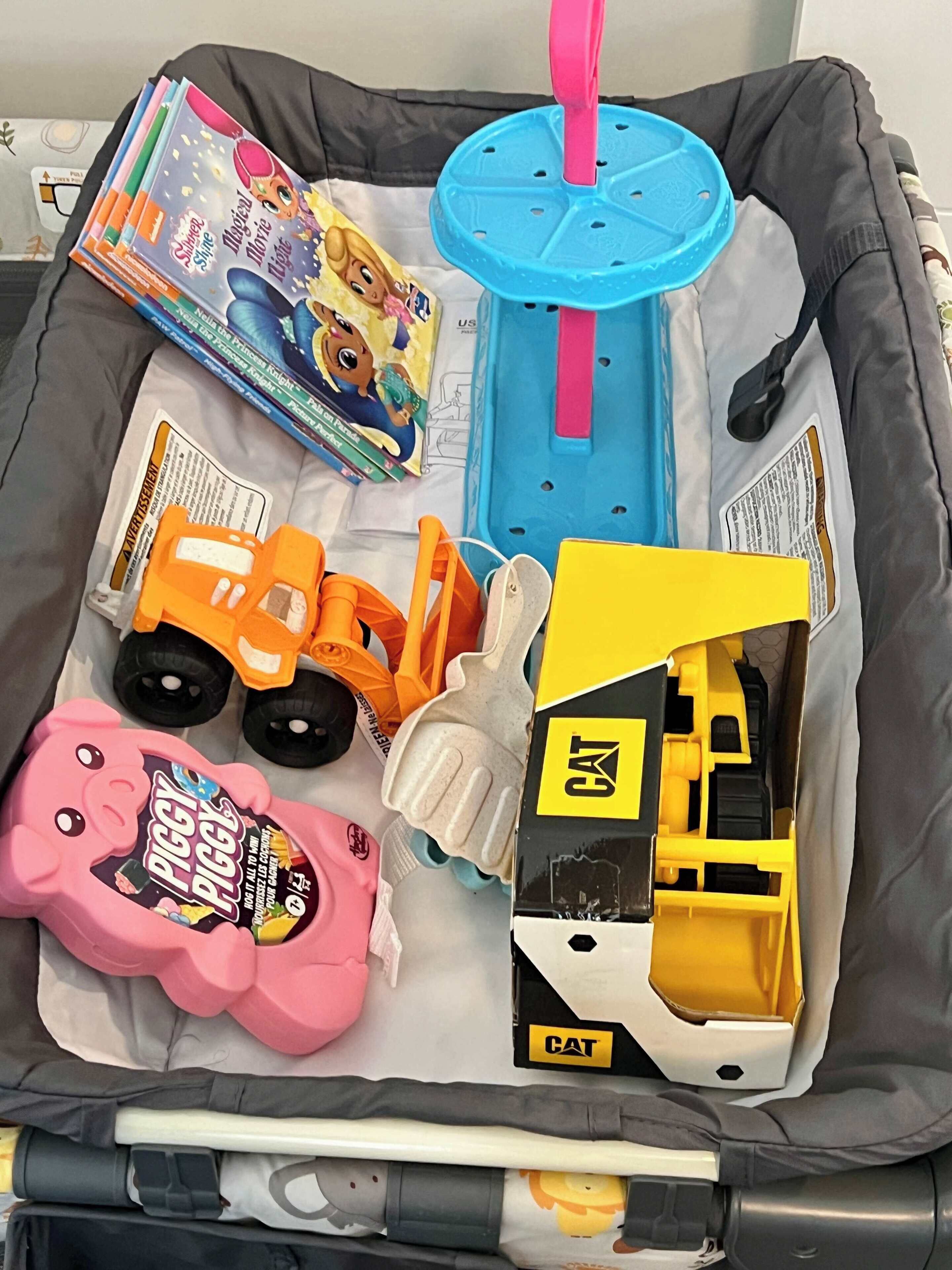 A travel bag containing a toy truck, a piggy bank, a toy construction vehicle, a toy hammer, and a toy shovel.