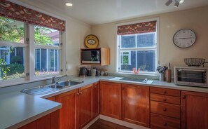 A kitchen with wooden cabinets, a sink, a microwave, and a clock on the wall.