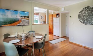 A dining area with a table set for four, a kitchen in the background, and a decorative wall piece.