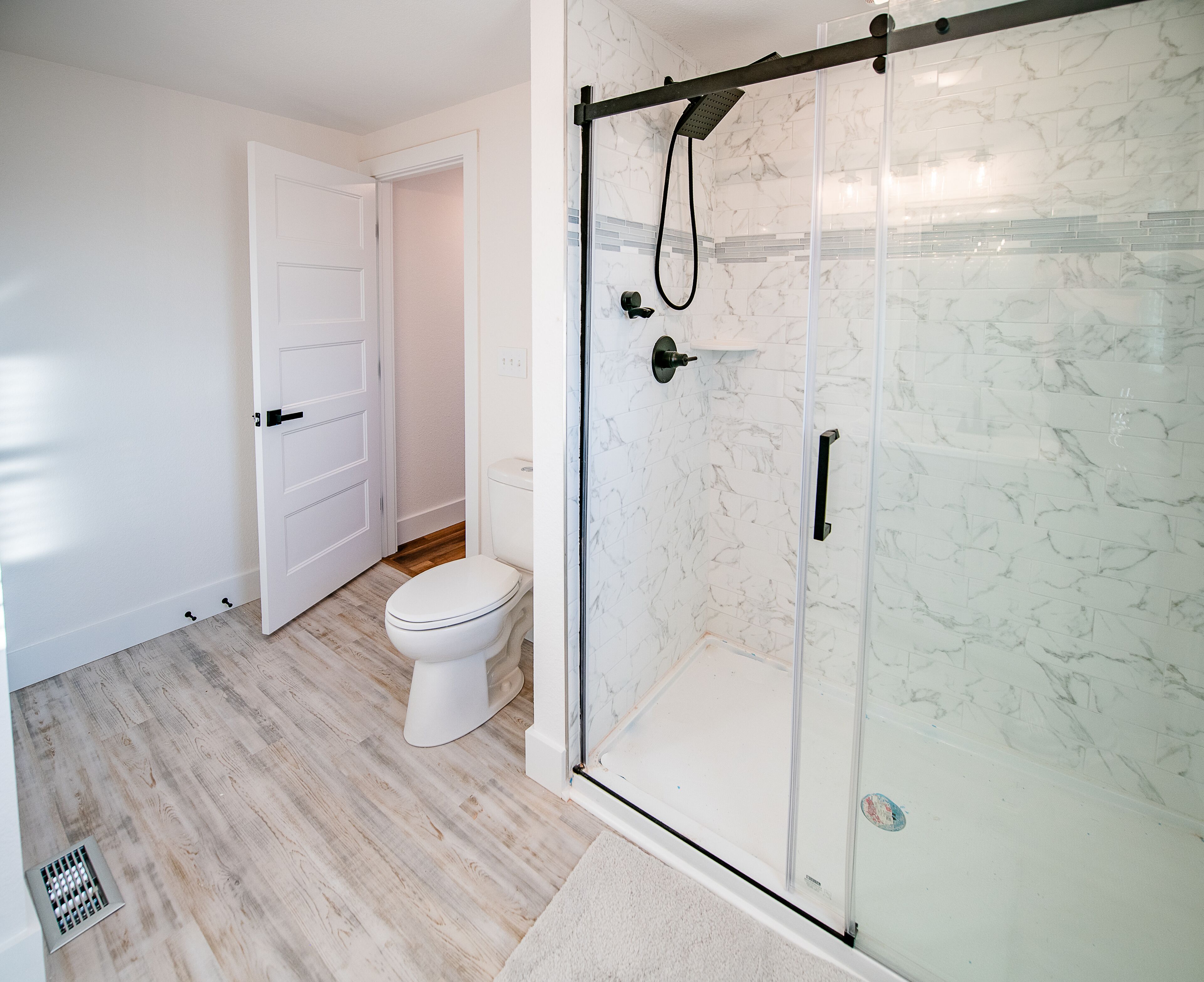 A modern bathroom with a glass-enclosed shower, a toilet, and a white door.